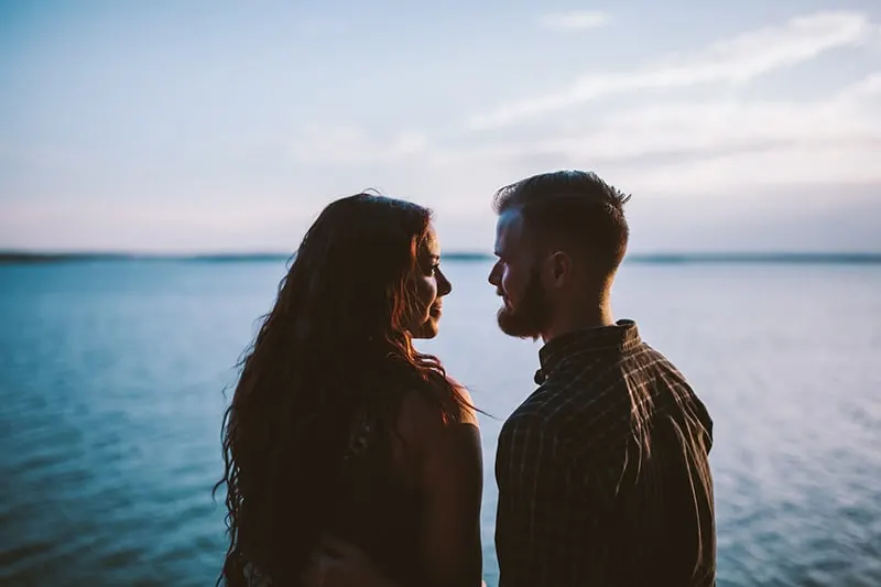 man and woman looking each other in eyes while standing near the body of water