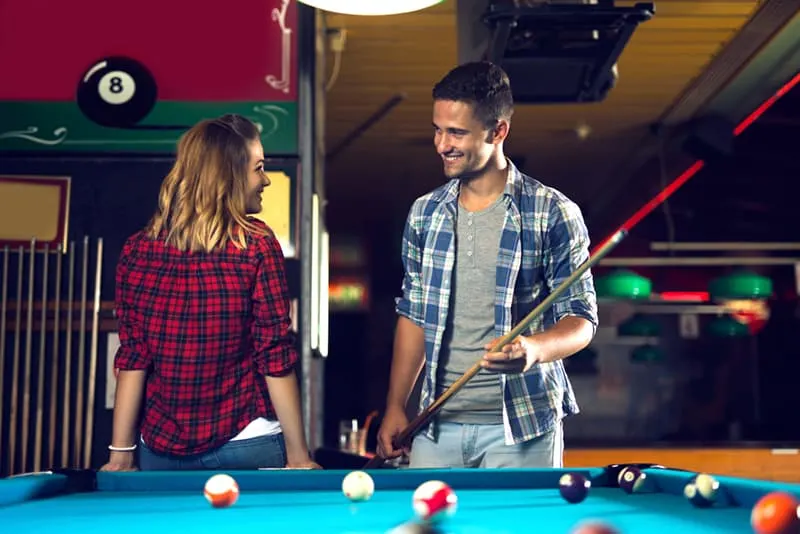 man and woman looking each other in eyes and flirting while playing billiard