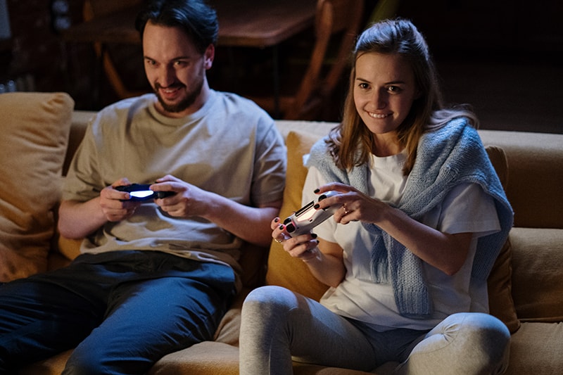 man and woman playing video games sitting on the couch