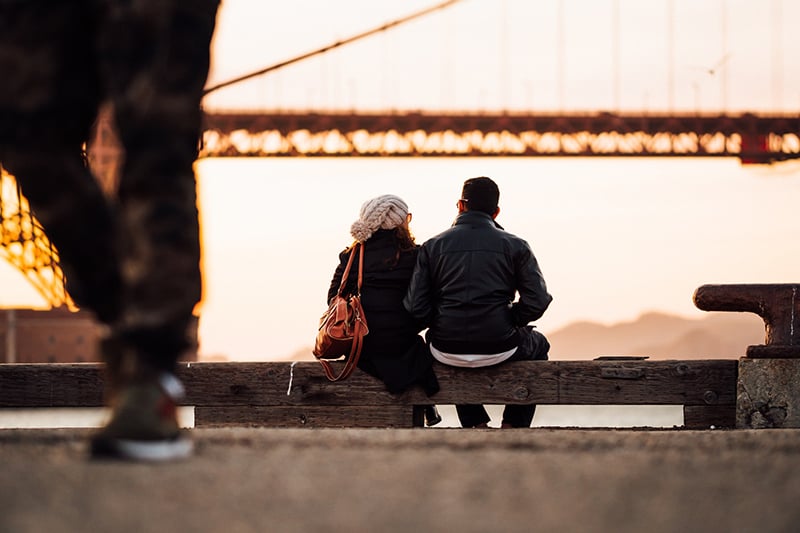 uomo e donna seduti su una panchina che osservano il tramonto