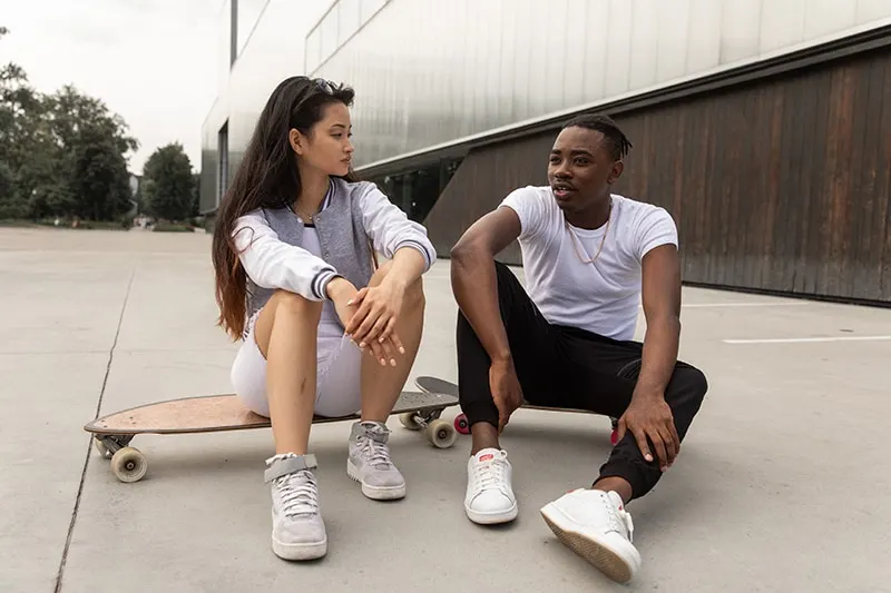man and woman talking while resting on skateboards after training