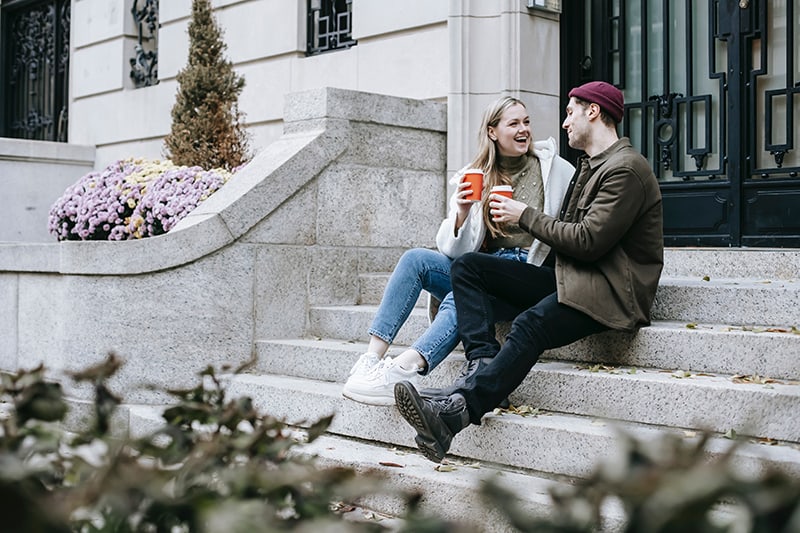 man and woman talking while drinking coffee on stairs