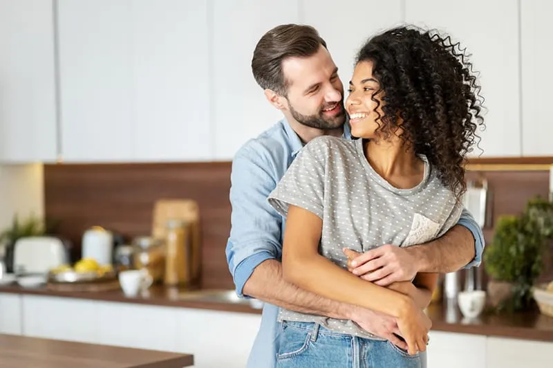 man embracing her wife from the back while standing in the kitchen