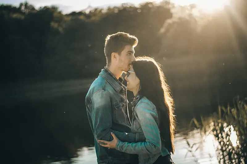 man kissing woman in the forehead while standing together near the lake