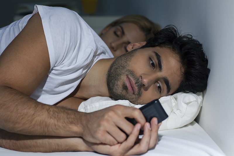 uomo che messaggia a tarda notte mentre la sua ragazza dorme accanto a lui