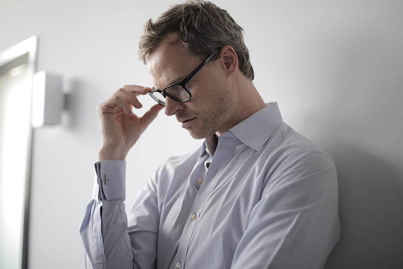 man touching eyeglasses with hand while leaning on the wall