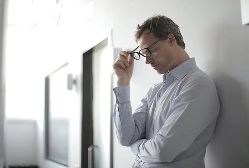 pensive man holding eyeglasses looking at floor