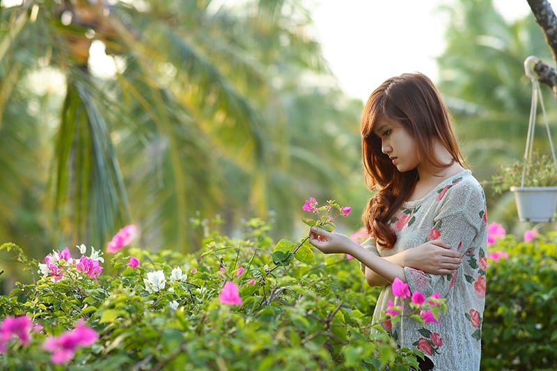 mulher pensativa a tocar em flores no jardim