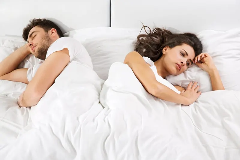 sad woman lying in the bed beside sleeping boyfriend