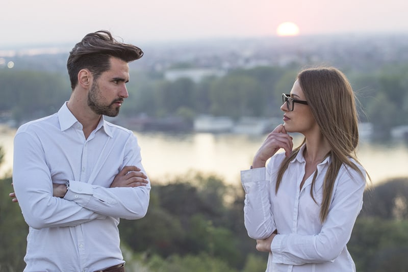 hombre y mujer serios mirándose de pie al aire libre