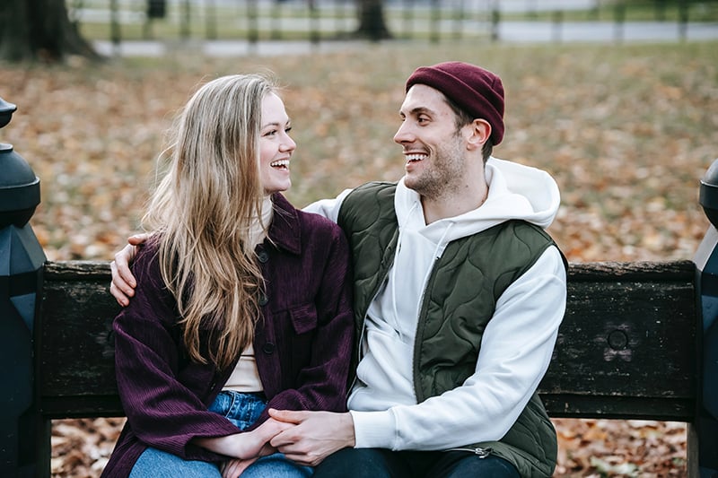 coppia sorridente seduta sulla panchina del parco che si tiene per mano