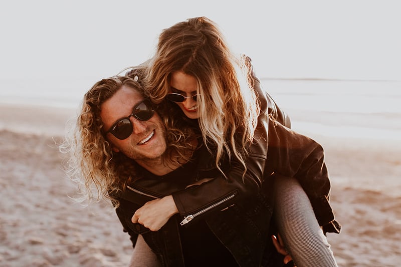 uomo sorridente che porta la sua ragazza sulla schiena sulla spiaggia