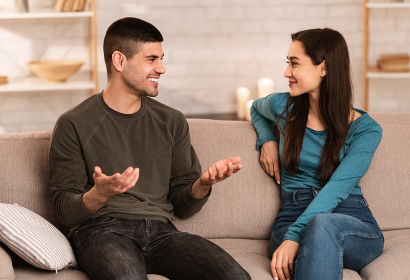 smiling man talking with his female friend while sitting on the couch