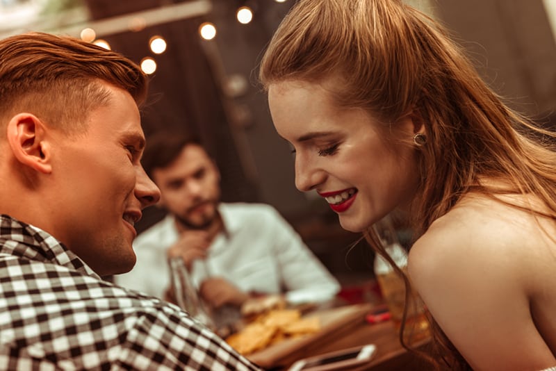 Donna sorridente che flirta con un uomo seduto vicino a lei in un ristorante