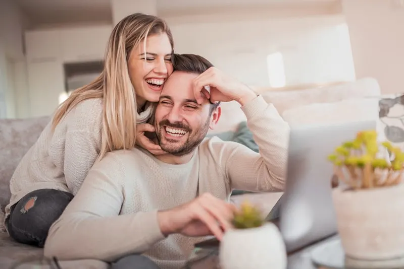 smiling woman hugging her smiling husband while sitting on the couch