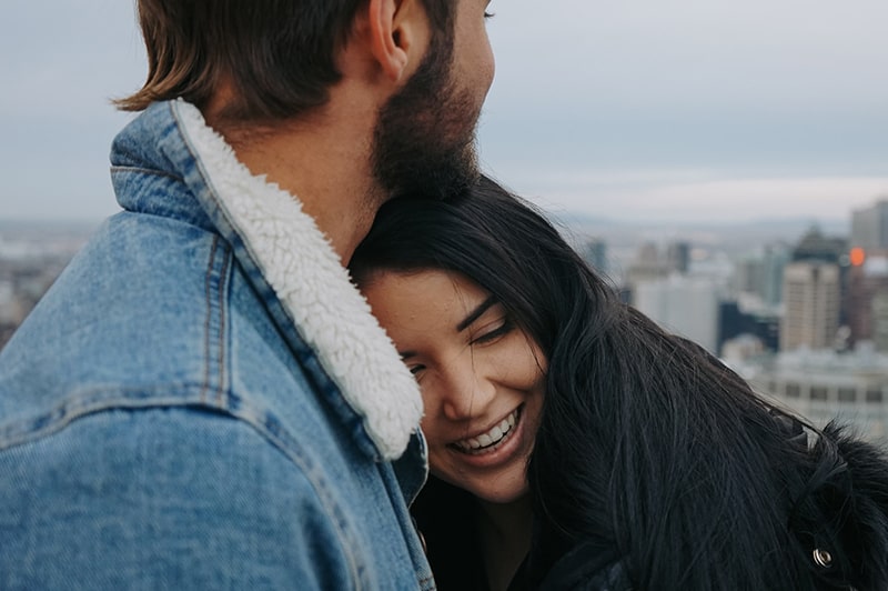 smiling woman leaning on her boyfriend's chest while standing on rooftop together
