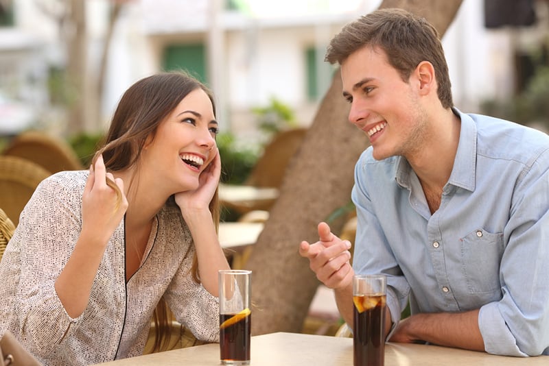 smiling woman looking a man in eyes while he flirting with her in cafe