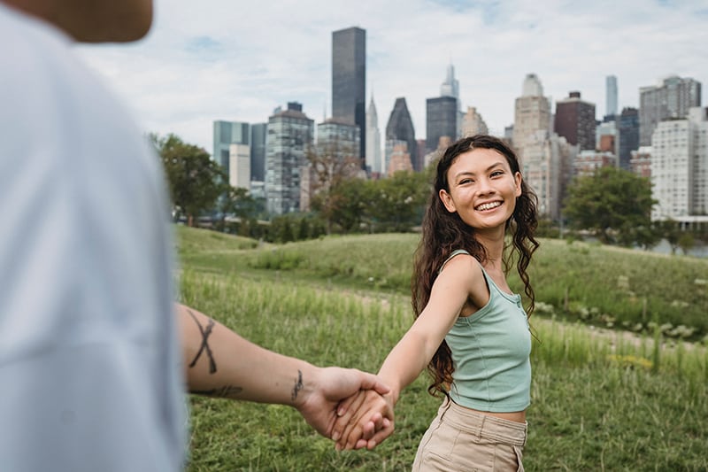 smiling woman turning to a man and holding his hand while walking on the grass field together