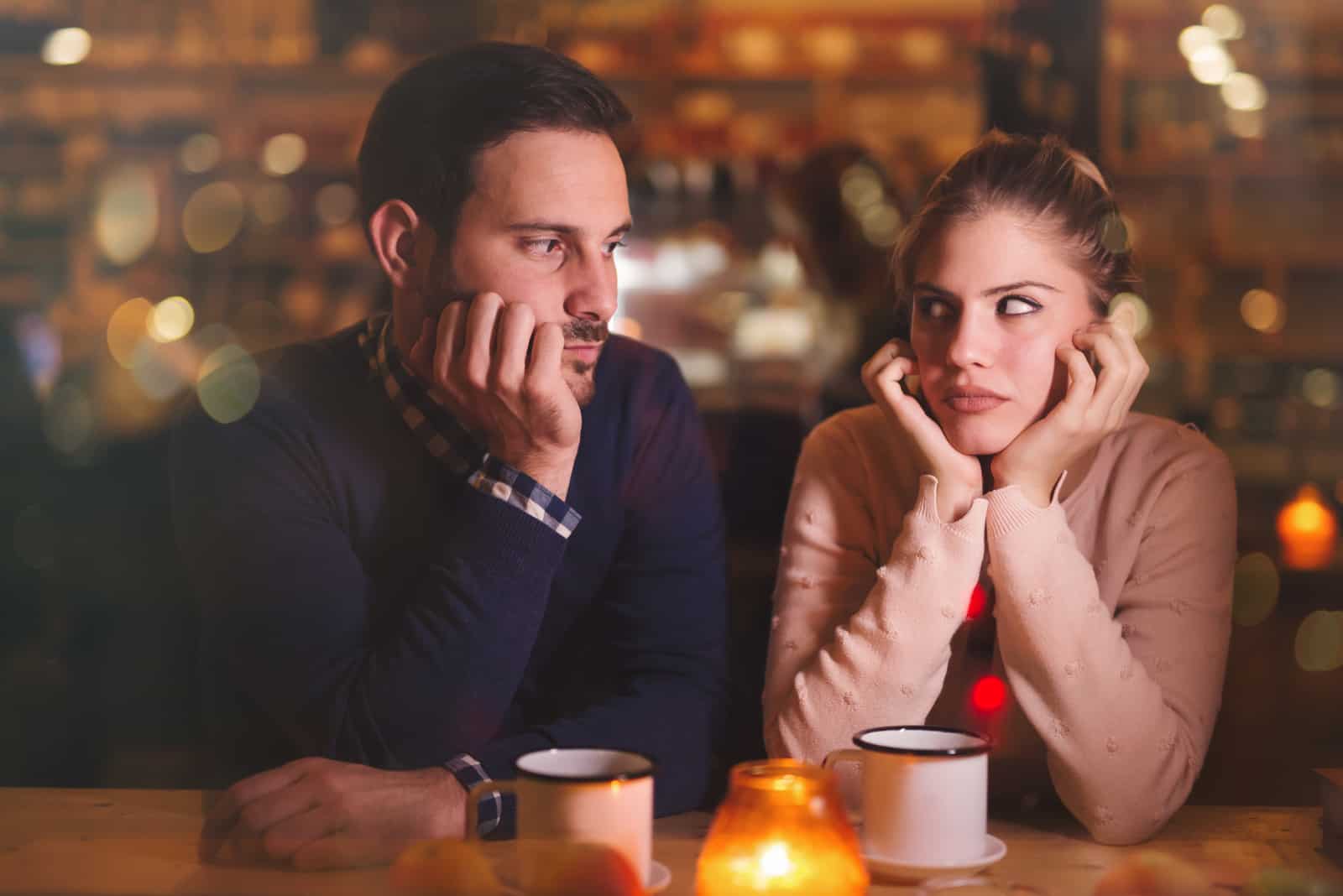 the man and woman sit at the table and look at each other confused