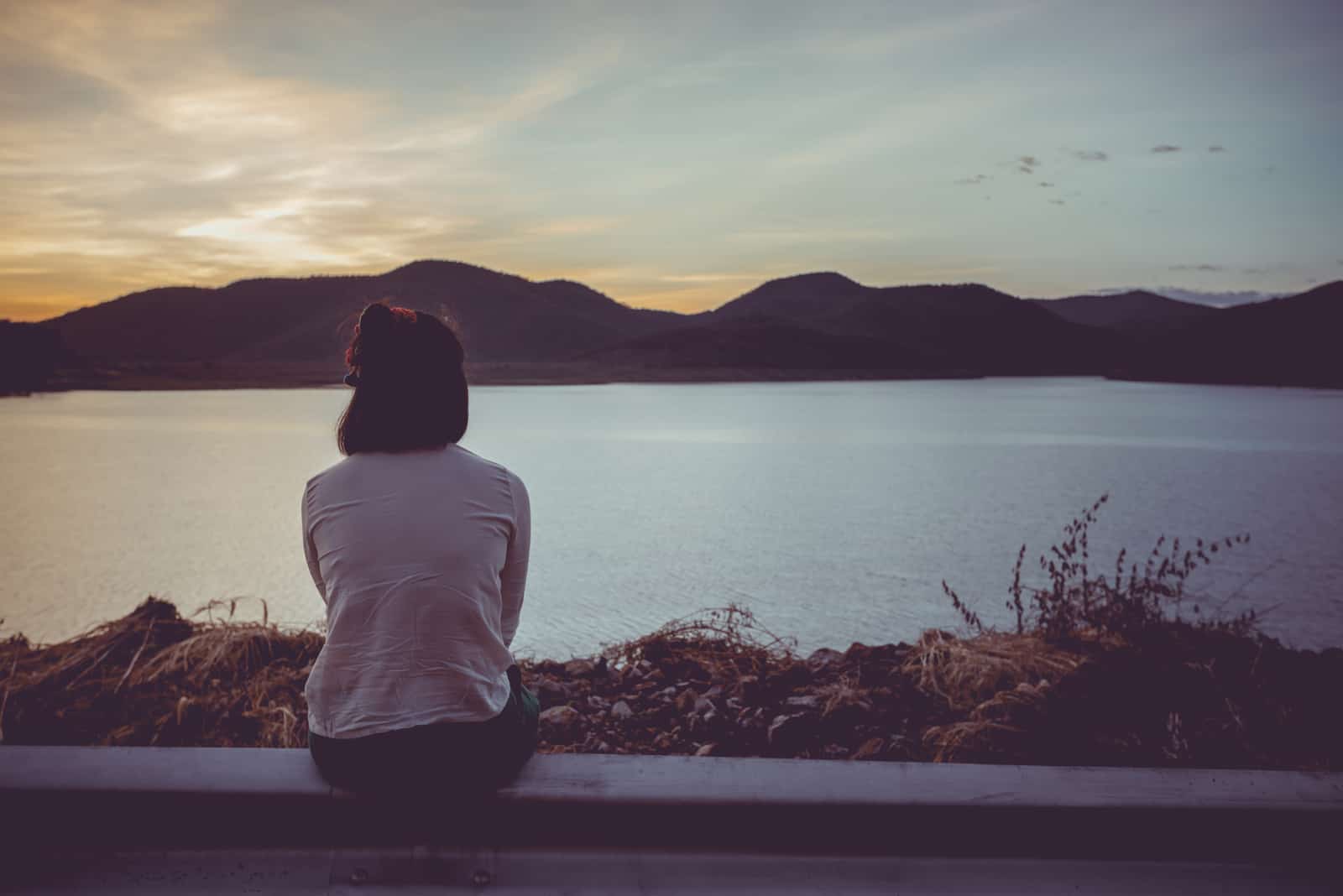 a mulher senta-se na vedação e olha para a distância