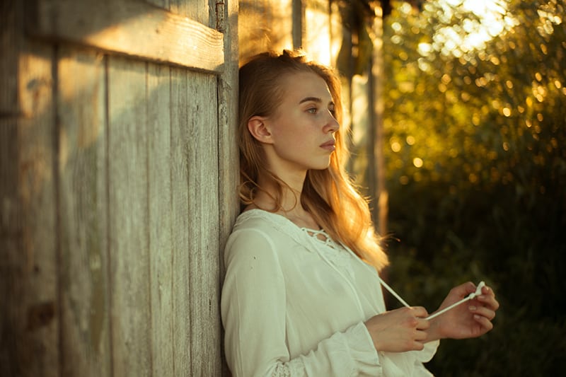 thoughtful woman leaning on wooden wall while standing outdoor