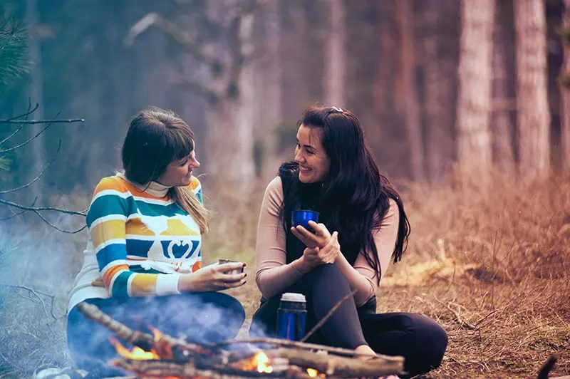 two women talking while sitting on the ground near campfire