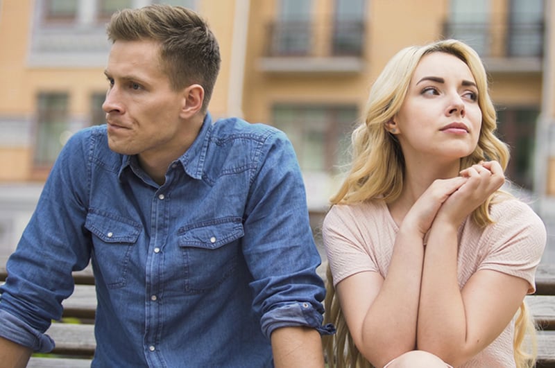 upset man turning from his girlfriend sitting on the bench close to him