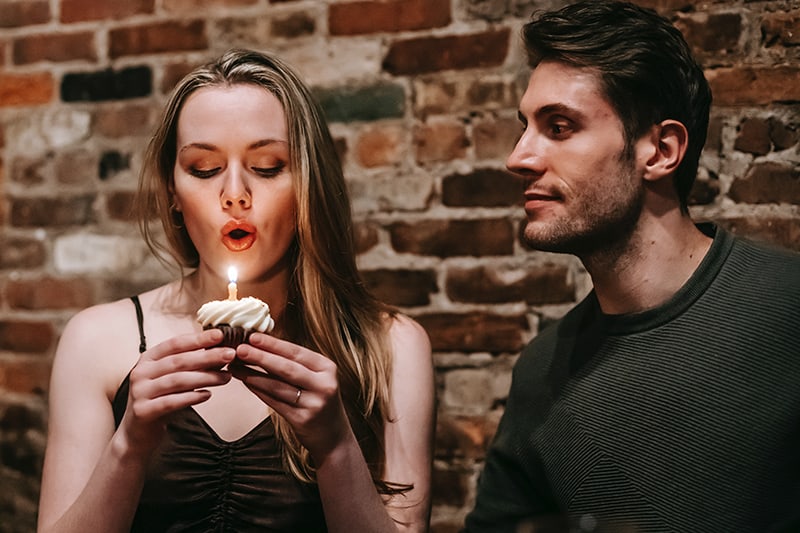 donna che soffia la candela su un biscotto mentre è seduta accanto al marito per festeggiare il primo anniversario insieme