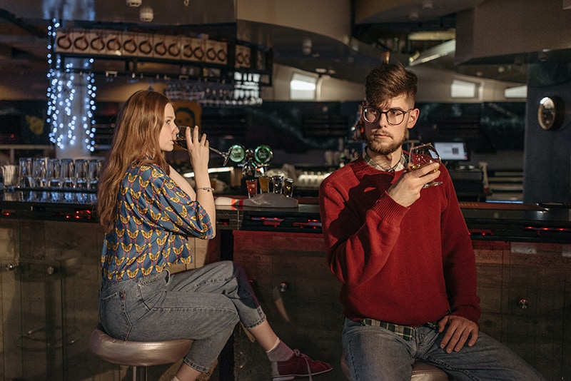 woman drinking wine looking at man sitting beside her in the bar