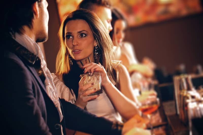 woman holding glass of drink and talking to a man standing beside her in the bar