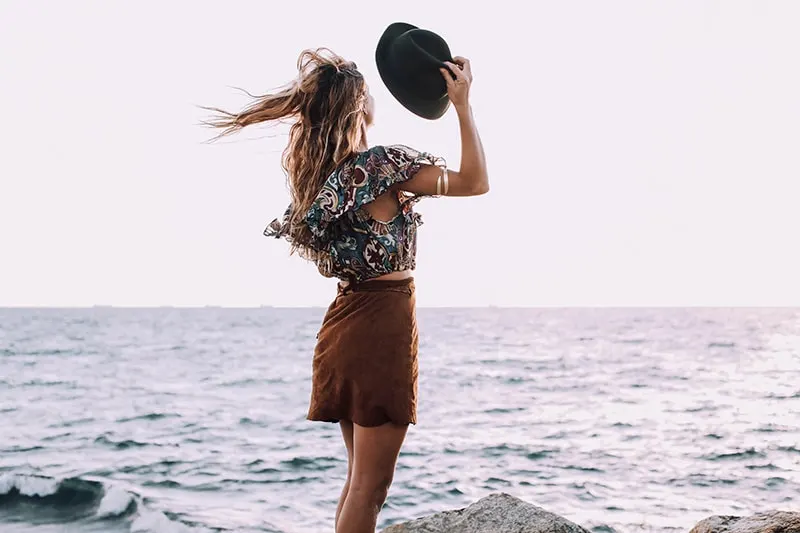 woman holding hat standing in the wind near the sea
