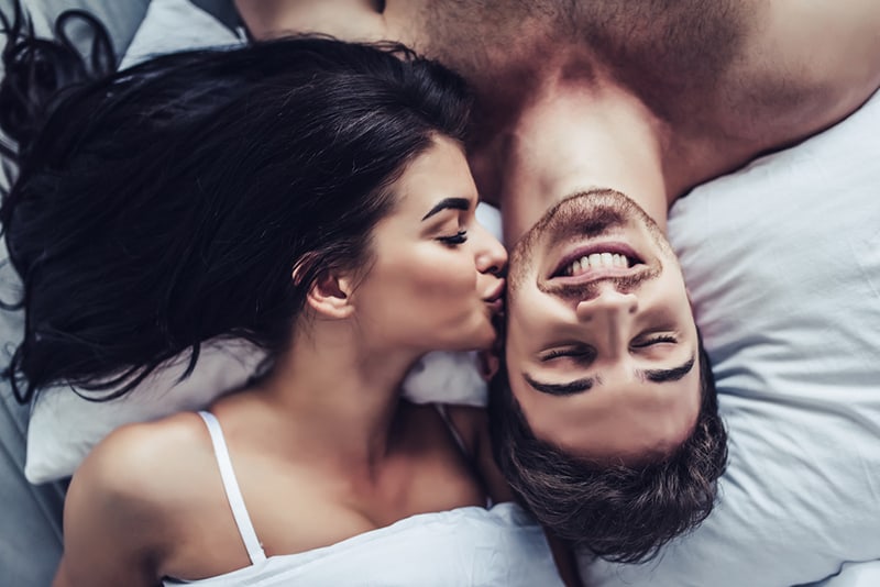 mujer besando a su novio en la mejilla mientras yacen juntos en la cama