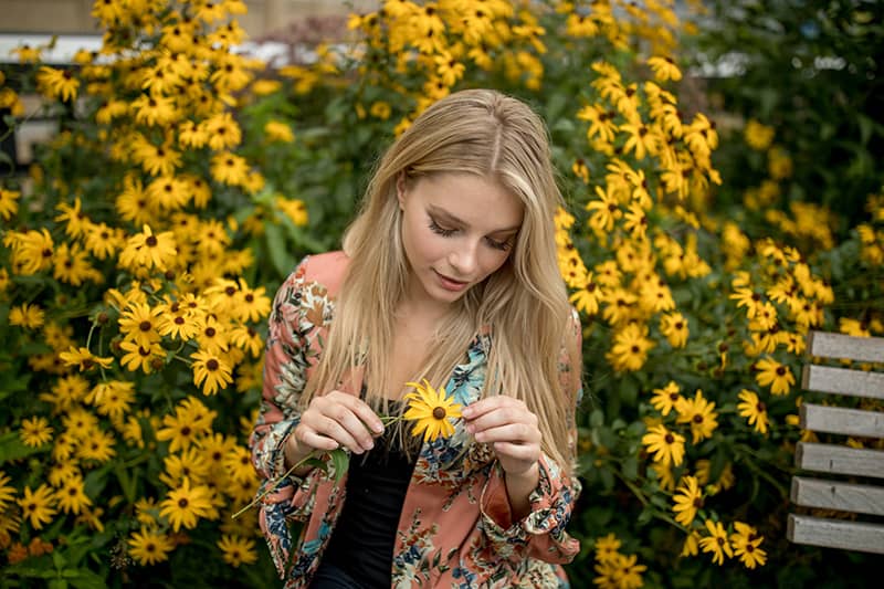 a woman surrounded with flowers holding one yellow flower