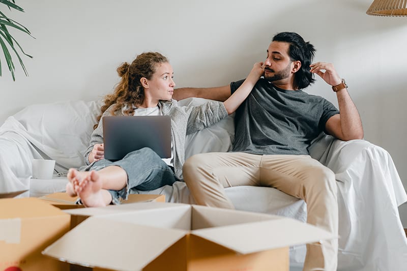 woman touching face of her boyfriend sitting near her on the couch