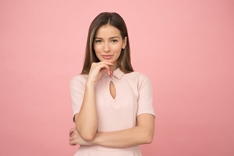 woman wearing a pink blouse touching chin with hand
