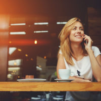 a smiling woman sits in a cafe and talks on the phone