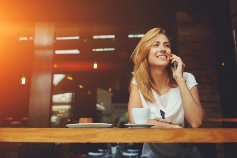 a smiling woman sits in a cafe and talks on the phone
