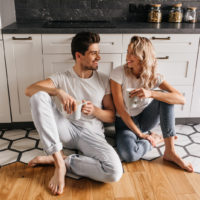 a man and a woman are sitting in the kitchen on the floor drinking coffee and talking