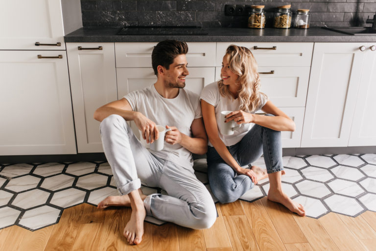 um homem e uma mulher estão sentados na cozinha, no chão, a beber café e a conversar