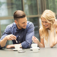 a smiling man and woman sit and drink coffee