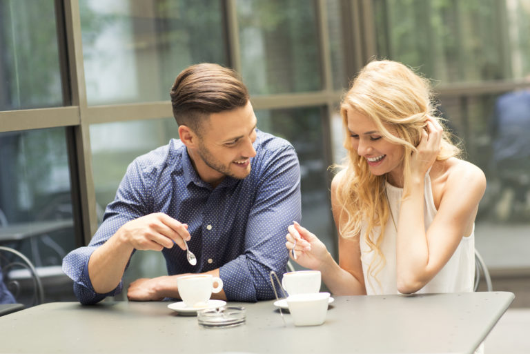 a smiling man and woman sit and drink coffee