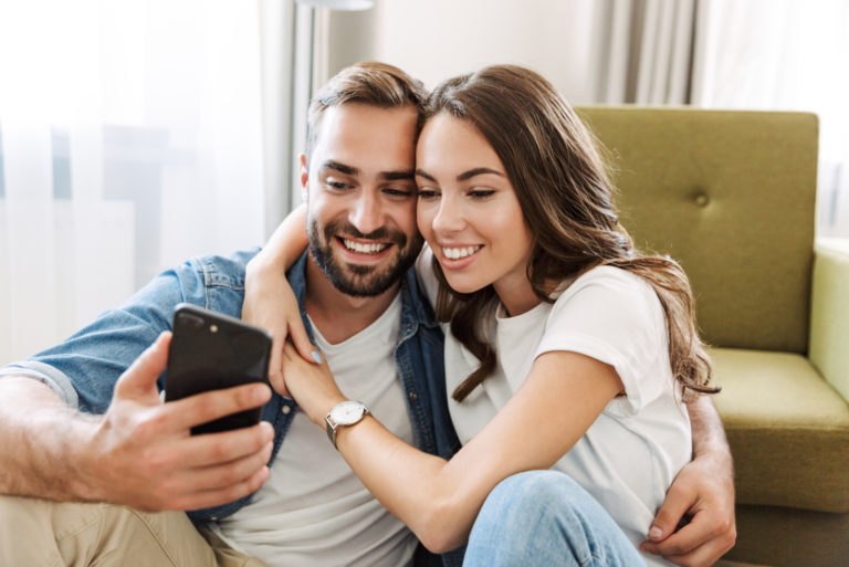 a smiling woman hugged a man and looked at the phone