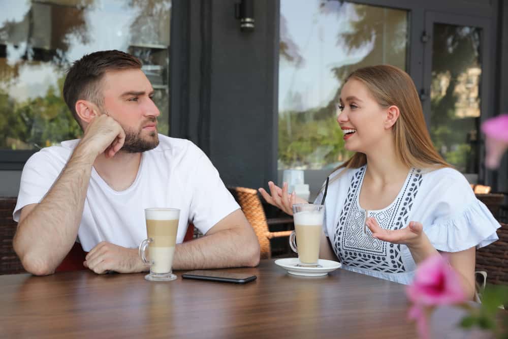 Young man having boring date with talkative girl in outdoor cafe