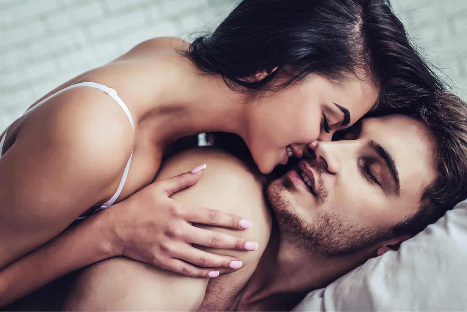 a beautiful black haired woman kisses a man in bed
