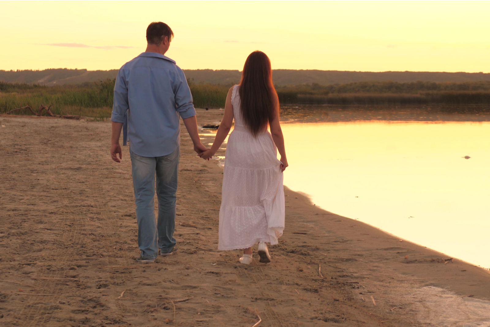 um homem e uma mulher caminham pela praia de mãos dadas