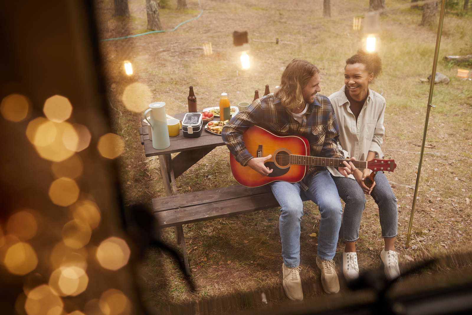 a man playing guitar a woman smiling sits next to him on a bench