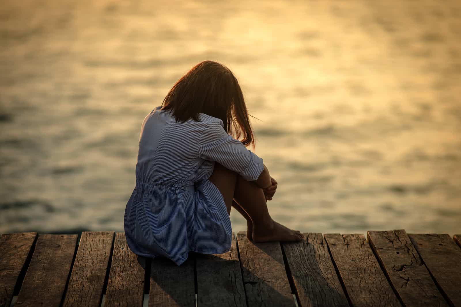 a sad woman with her head down sits on the pier