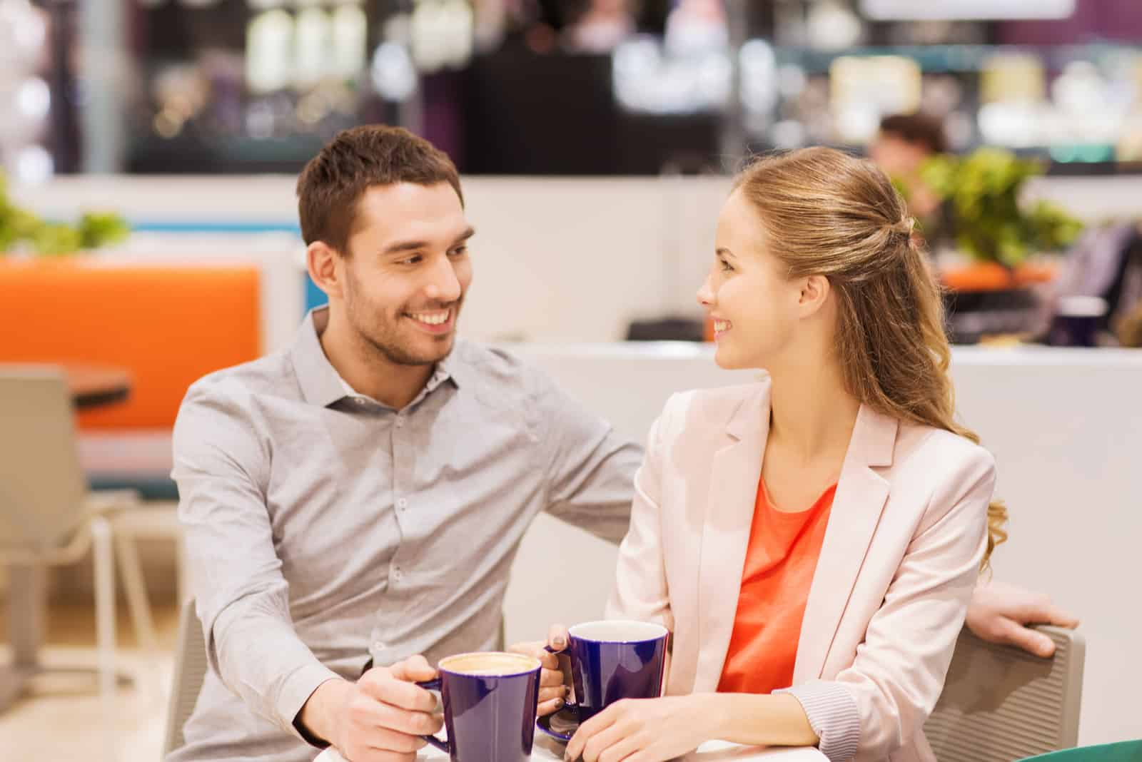 a smiling man and a woman sit at a table and drink coffee