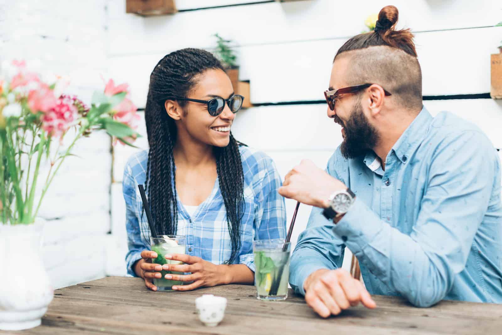 a smiling man and a woman sit at a table drinking drinks and looking at each other