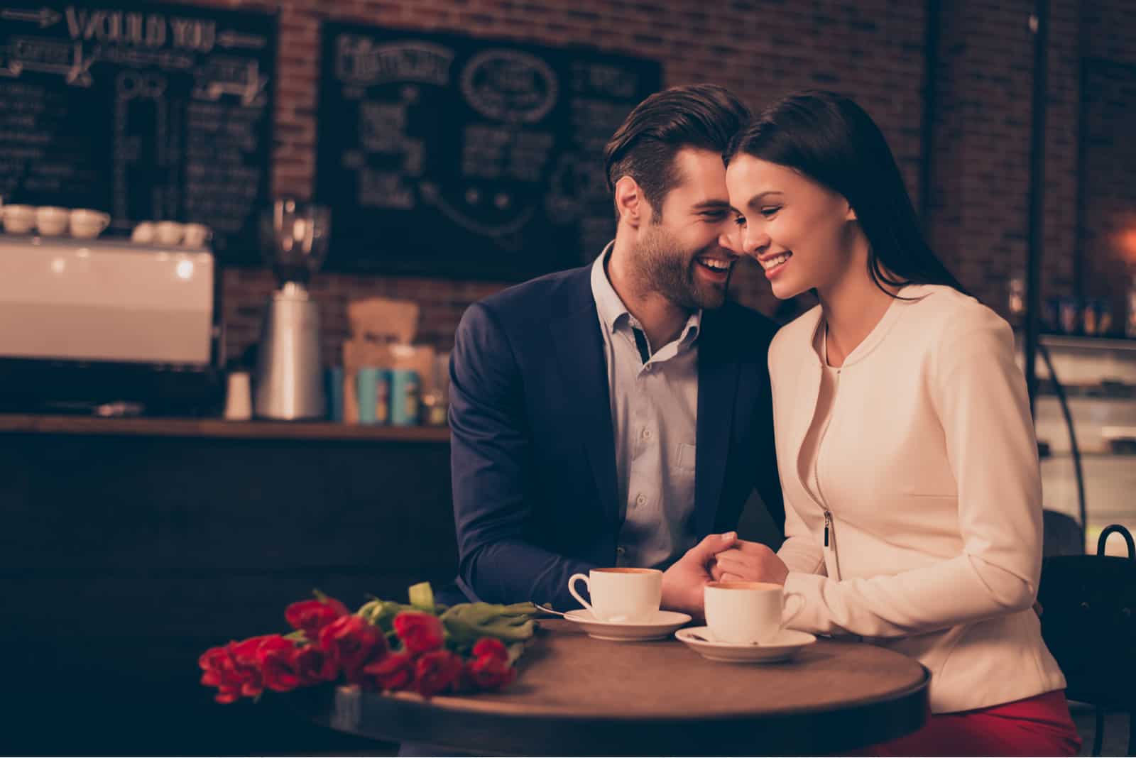 un hombre y una mujer sonrientes cogidos de la mano sentados a la mesa
